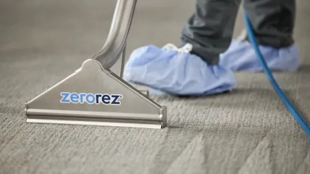 Professional carpet cleaning with Zerorez tool and technician wearing blue shoe covers on grey carpet.