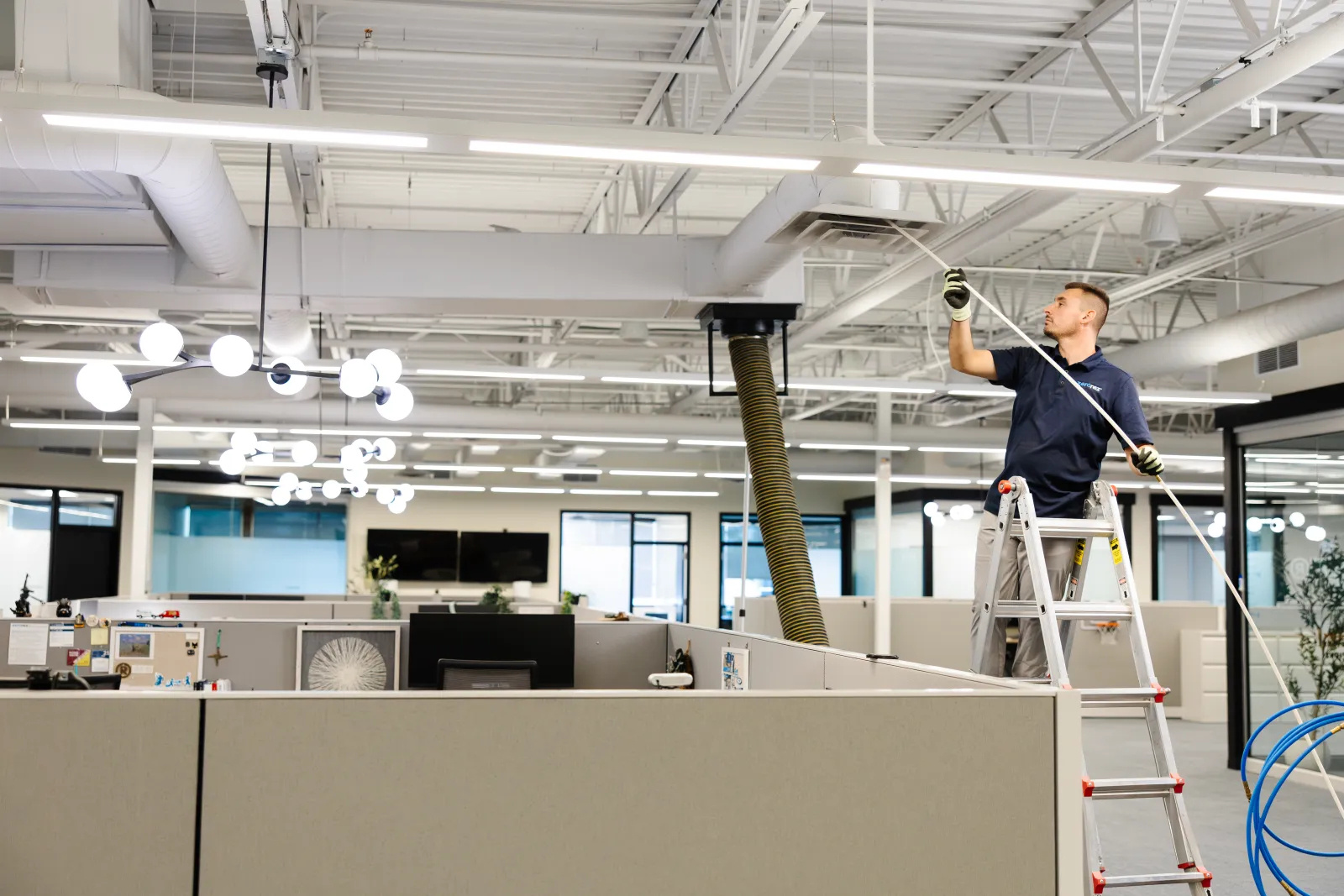 air duct cleaning in an office space with a technician on a ladder